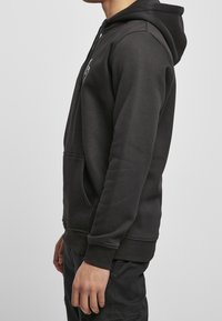 Felpa nera in misto cotone, con tasca frontale, cappuccio regolabile, polsini a costine e dettagli del logo minimalista sul petto.