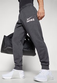 Grå joggers med elastisk talje, med et reflekterende Nike-logo. Sammen med hvide sportssko og en sort gymnastiktaske.