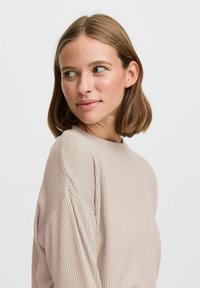 Light beige ribbed sweater with a round neckline and dropped shoulders. Soft texture and relaxed fit, highlighting the fabric's subtle pattern.