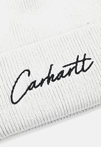 Weißer gerippter Beanie mit schwarzem, gesticktem "Carhartt"-Logo. Das Material hat ein strukturiertes Muster, das das Strickdesign betont.