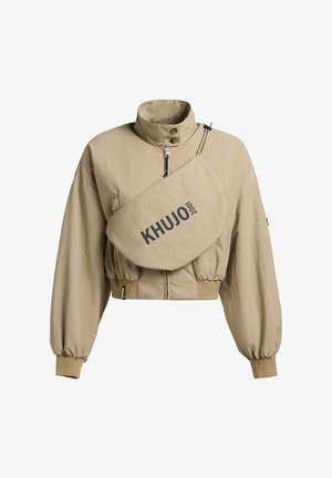 Jachetă bej scurtă, cu guler înalt, manșete elastice, fermoar frontal și buzunar diagonal mare pe piept, inscripționat cu "KHUJO 2001".