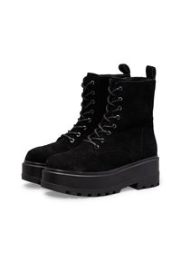 Botas de tobillo de ante negro con suela de plataforma gruesa, puntera redonda y ojales reforzados. Cuentan con un cierre de cordones en la parte delantera y una tira en la parte posterior para un fácil calzado.