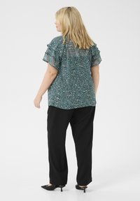 Blusa de color verde azulado con estampado y mangas con volantes, combinada con pantalones negros de pierna ancha y tacones negros de punta. Tela ligera y fluida.