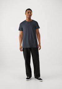 Tricou din bumbac de culoare albastru închis, cu mâneci scurte, asortat cu o pereche de pantaloni negri din denim mulați și adidași negri. Model care poartă ochelari de soare cu lentile aurii.