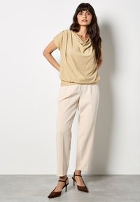 Złota bluzka z krótkimi rękawami, w połączeniu z beżowymi spodniami w kant i brązowymi szpilkami z ostrym noskiem. Gładka tekstura z delikatnym połyskiem.