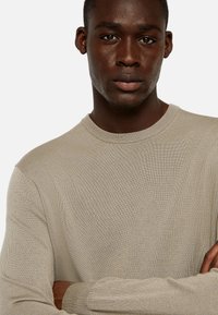 Light beige ribbed long-sleeve sweater with a crew neck. Soft texture, fitted design, and prominent stitching details on the cuffs and hem.