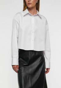 Hvid kort skjorte med knapper, klassisk krave, lange ærmer og en struktureret pasform, kombineret med en sort lædernederdel.