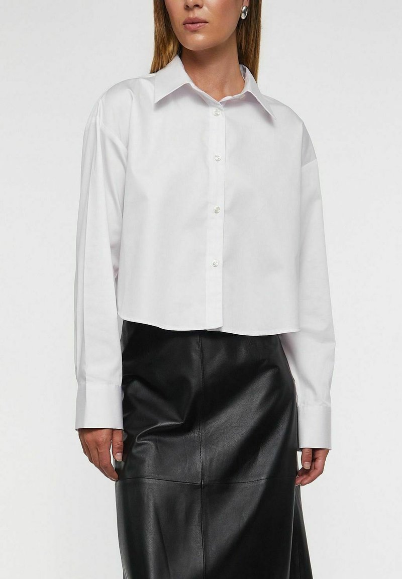Hvid kort skjorte med knapper, klassisk krave, lange ærmer og en struktureret pasform, kombineret med en sort lædernederdel.
