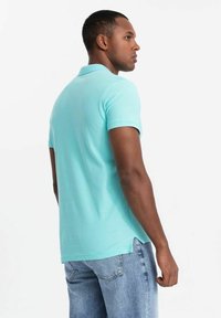 Ljusblå polo-shirt i bomull med klassisk krage, korta ärmar och sidofickor. Bärs tillsammans med blekta blå jeans.