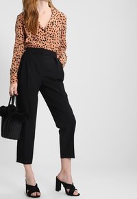 Kragskjorta i en peachfärgad, leopardmönstrad tyg; kombinerad med högmidjade svarta byxor. Svarta klackar med blockklack och en texturerad handväska.