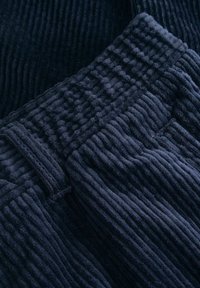 Marineblauwe corduroy stof met verticale ribbelstructuur, met een gladde tailleband en stikseldetails over de stukken.