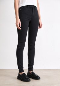 Zwarte skinny jeans van denim, met een gladde textuur, een strakke pasvorm en voorzakken. Draagt met zwarte textured loafers.