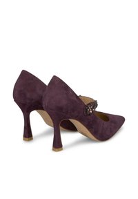 Scarpe con tacco alto in suede viola, con punta appuntita e una fascia decorativa accentuata da pietre. L'altezza del tacco è moderata e presenta una finitura testurizzata.
