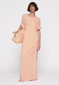 Abito maxi pesco con maniche corte e vestibilità rilassata, caratterizzato da uno spacco laterale e un tessuto morbido. Abbinato a una borsa a tracolla beige coordinata.