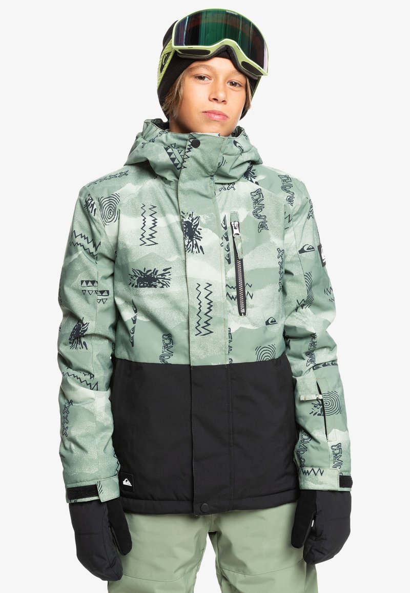 Zielono-czarna kurtka śniegowa w wzory z zamykaną kieszenią, wyposażona w kaptur i czarne rękawice, noszona przez osobę na białym tle.
