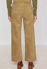 Pantaloni in corduroy a gamba larga di colore marrone chiaro, con righe verticali, vita alta e due tasche posteriori. Il modello indossa stivali marroni con tacco.