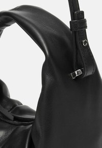 Borsa a tracolla in pelle nera con una superficie morbida e testurizzata, caratterizzata da una maniglia arrotondata e un accento in metallo argentato.