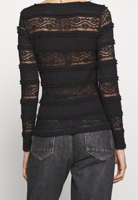 Schwarzes Langarmoberteil mit geschichteter, transparenter Spitze und strukturierten Streifen, runder Halslinie und gerippten Akzenten. Kombiniert mit Jeans.