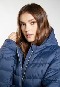 Giacca a vento blu navy con cappuccio, dotata di zip argentata, texture trapuntata e polsini elasticizzati, che offre calore e comfort.