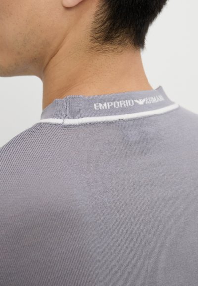 Maglietta grigia a coste con un colletto bianco, caratterizzata da un logo sul retro—"EMPORIO ARMANI"—che evidenzia il suo design di marca.