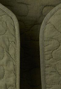 Gros plan sur un tissu matelassé vert olive avec des coutures courbes et des bords rembourrés créant un motif symétrique.