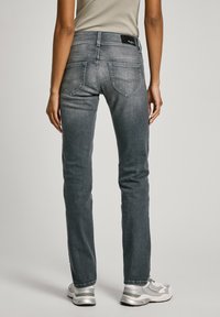 Šedé džínové kalhoty mají přiléhavý střih, zadní kapsy s dekorativním šitím a černou značkovou nášivku na pásku. Stříbrné tenisky dotvářejí outfit.