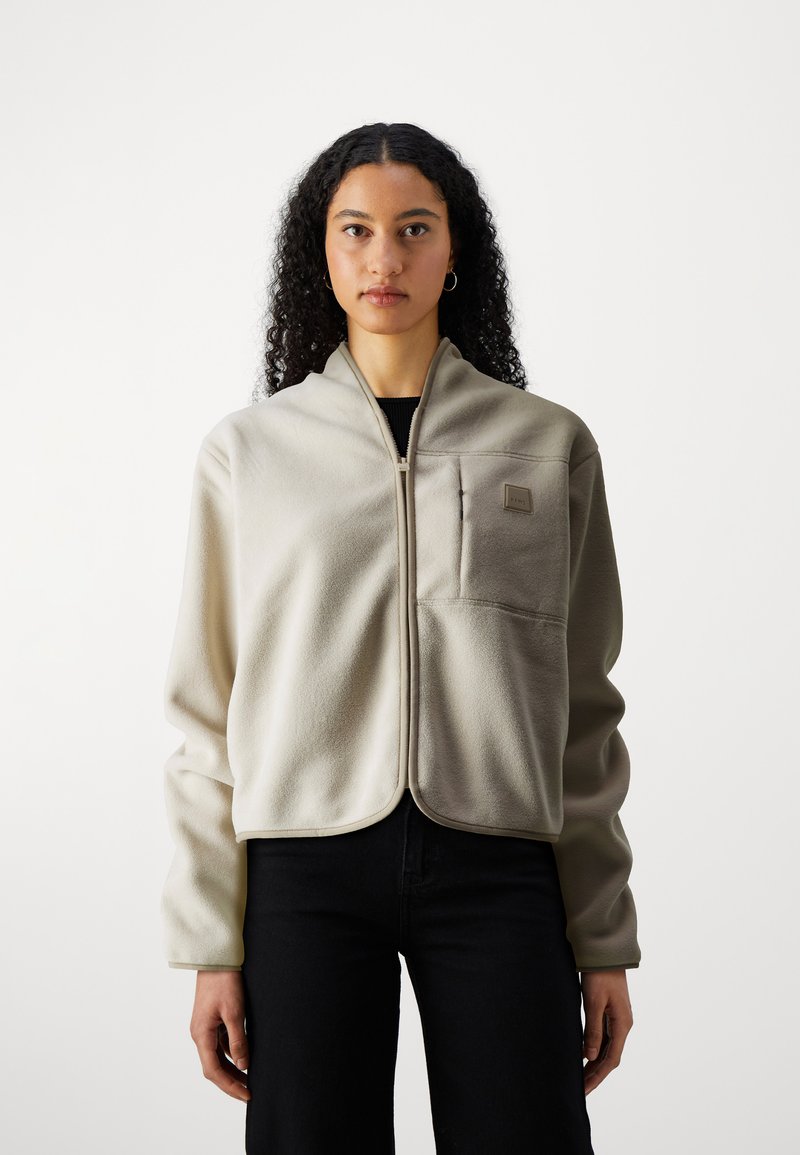 Lichtbeige fleece jas met een staande kraag, voorrits en een borstzak. Kenmerkt zich door een zachte textuur en een reguliere pasvorm.