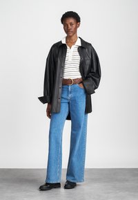 Black leather oversized shirt jacket over a striped polo shirt, paired with light blue wide-leg jeans and a braided brown belt. Black ankle boots.