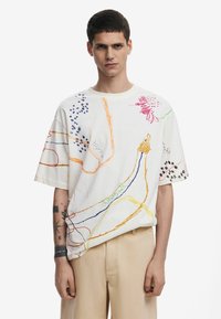 T-shirt bianca in cotone con ricami multicolori in diversi motivi, tra cui righe e design floreali, con maniche corte e vestibilità comoda.