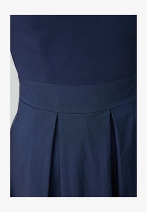 Le tissu de la robe marine présente un corsage ajusté avec une texture lisse et un détail de jupe plissée à la taille, mettant en valeur un design sur mesure.