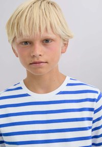Camisa blanca de manga larga con rayas azules horizontales; textura suave; cuello redondo; llevada por un niño con cabello rubio corto y ojos azules.
