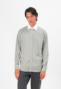 Grønn og hvit stripete skjorte med stiv hvit krage, har lange ermer og en liten brodert detalj nær sømmen.