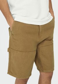 Brune cargo shorts lavet af holdbart materiale, med to sidelommer og en venstre værktøjslomme, i en lige pasform og med syninger.
