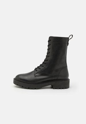 Black leather ankle boot with a rounded toe, lace-up front, and pull tab. Features a textured upper and chunky rubber sole.
