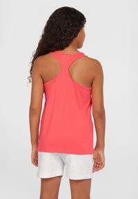 Korallenfarbenes Tanktop mit Racerback-Design, aus weichem Material gefertigt. Kombiniert mit hellgrauen Shorts im entspannten Schnitt.