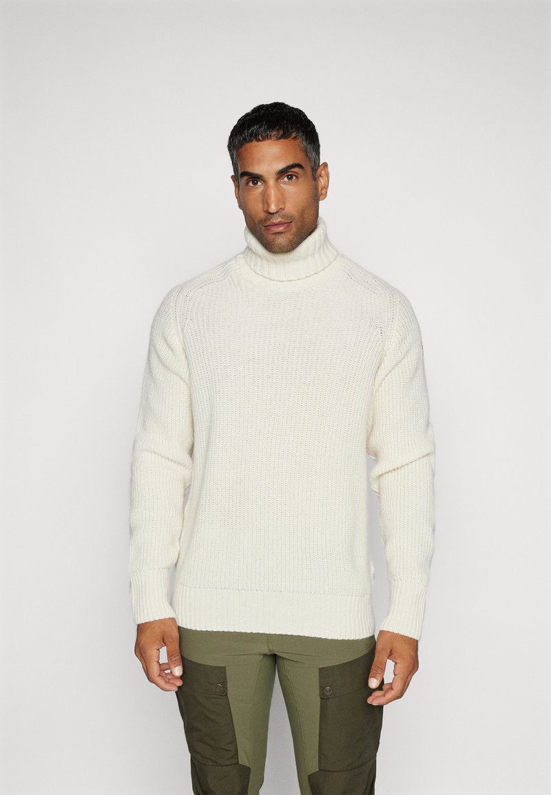 Maglione bianco a collo alto lavorato a maglia, con dettagli a coste su polsini e orlo, abbinato a pantaloni cargo verde oliva con tasche a pattina.