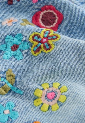 Colorful embroidered flowers in red, yellow, blue, and pink on light blue denim fabric with visible texture and stitching.