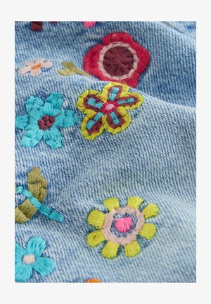 Bunte bestickte Blumen in Rot, Gelb, Blau und Rosa auf hellblauem Denim-Stoff mit sichtbarer Textur und Naht.