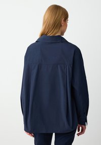 Navy blue cotton shirt featuring a relaxed fit, pointed collar, and long sleeves with buttoned cuffs; plain design with minimal detailing.