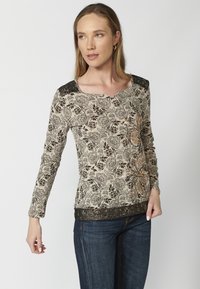 Langarmoberteil in Beige mit schwarzem Blumenmuster. Verfügt über einen strukturierten schwarzen Spitzenkragen und dekorative Blumendetails in Orange.