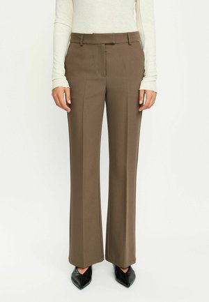 Pantaloni maro croiți, cu un design drept, curea de brâu și buzunare frontale, asortați cu tocuri negre ascuțite. Textură de țesătură netedă.