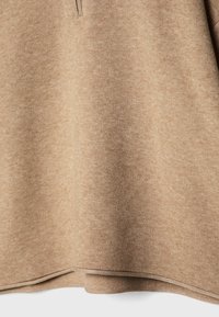 Brązowa bluza z teksturowanej, miękkiej tkaniny. Posiada okrągły dół oraz subtelne przeszycie wzdłuż krawędzi. Widok z góry.