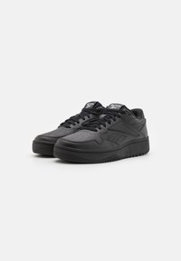 Black leather sneakers with a textured surface, round toe, perforated accents, and flat laces; featuring a thick rubber sole.