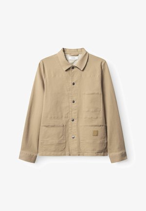 Beežist lõuendist jakk, millel on krae, ees nööbitav sulgemine, kaks suurt eesmist taskut ja väikene logomärk alumise tasku peal.