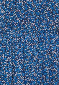 Gros plan sur un tissu bleu avec un petit motif floral composé de fleurs bleues et blanches aux centres orange sur un tissu froncé.