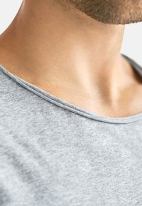 Ljusgrå bomulls T-shirt med ribbad rundad halsringning och mjuk textur, som visar en del av hals- och axelområdet.
