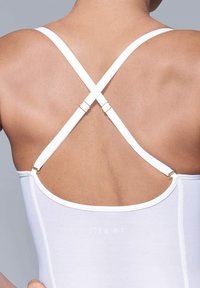 Weißer Body mit einem über Kreuz verlaufendem Rückendesign, verstellbaren Trägern und goldfarbenen Hardware-Details. Glatte Textur mit minimalem Branding.