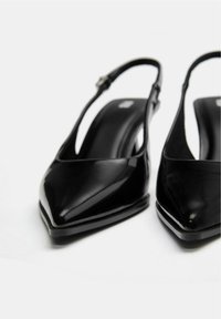 Pantofi slingback din piele lacuita neagra, cu varfuri ascutite, finisaj lucios si barete reglabile la glezna. Se caracterizeaza prin talpi texturate pentru aderenta.