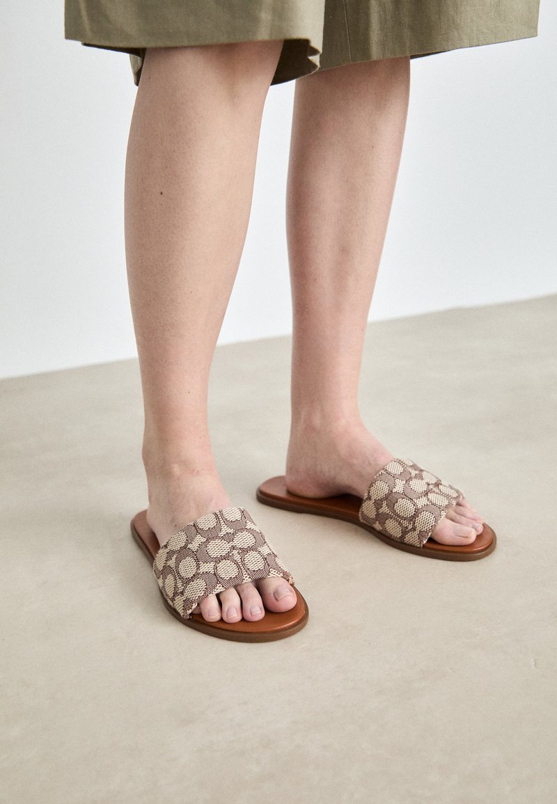 Bruine schuifsandalen met een getextureerde strap in bruin en beige patroon. Platte zool met een gladde afwerking, waardoor de blootgestelde tenen zichtbaar zijn. Eenvoudig ontwerp.