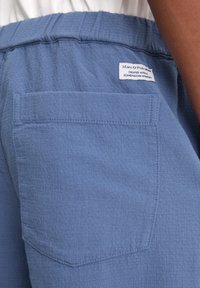Blauwe stoffen shorts met een elastische tailleband en een achterzak. Een label zegt: "Marc O'Polo, ontworpen met een Scandinavische mindset."